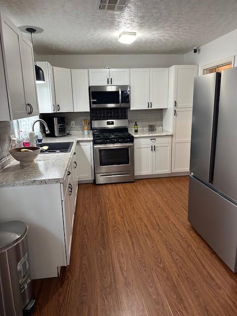 kitchen with dark wood finished floors, light countertops, appliances with stainless steel finishes, white cabinets, and a textured ceiling