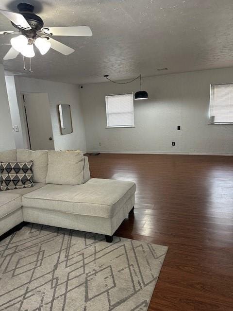 living room featuring a ceiling fan, a textured ceiling, baseboards, and wood finished floors