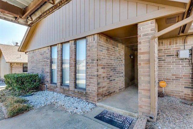 doorway to property featuring board and batten siding and brick siding