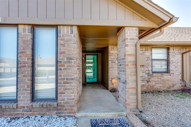 view of exterior entry with a shingled roof and brick siding