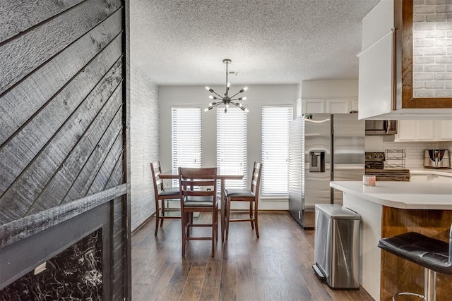 dining room featuring dark wood-style floors, brick wall, a textured ceiling, and an inviting chandelier