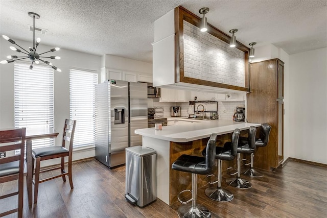 kitchen featuring stainless steel appliances, a peninsula, visible vents, light countertops, and dark wood finished floors