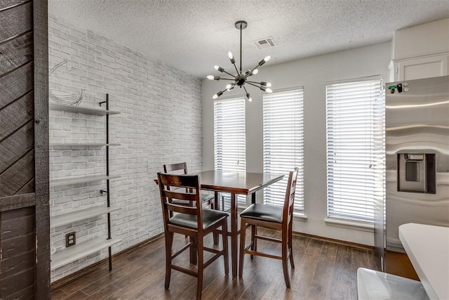 dining area featuring a chandelier, a textured ceiling, brick wall, wood finished floors, and visible vents