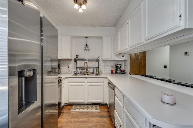 kitchen with stainless steel appliances, a sink, white cabinets, backsplash, and dark wood finished floors