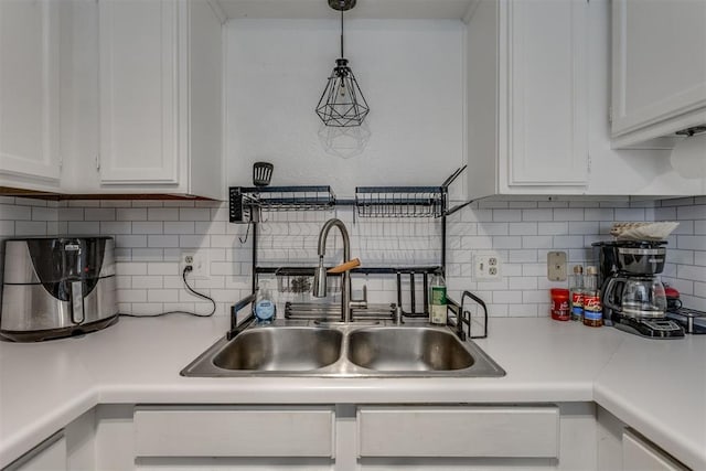 kitchen featuring decorative light fixtures, light countertops, backsplash, white cabinets, and a sink