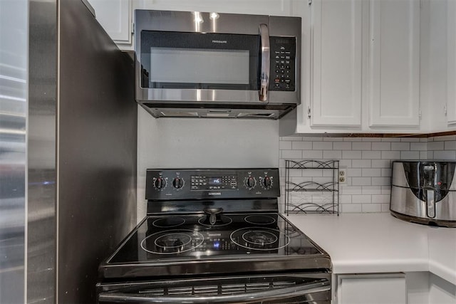 kitchen featuring stainless steel microwave, freestanding refrigerator, black electric range, white cabinetry, and backsplash