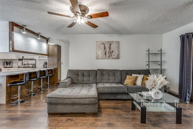 living area with ceiling fan, a textured ceiling, and dark wood-style flooring