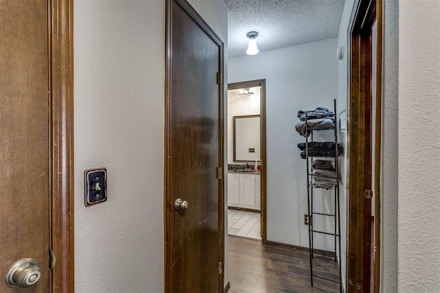 hallway featuring a textured ceiling, a textured wall, a sink, and dark wood finished floors