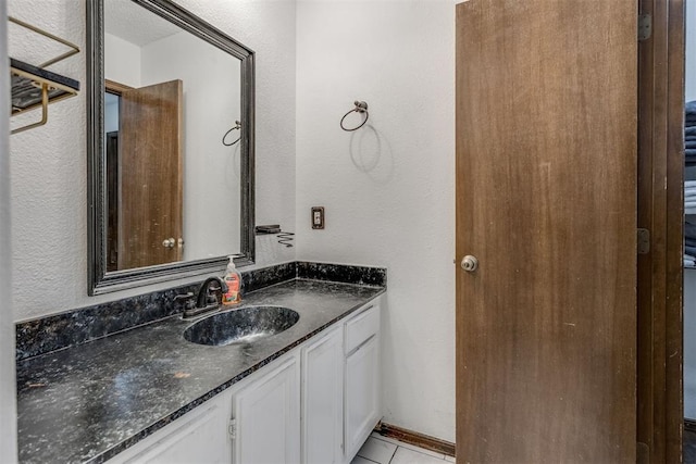 bathroom with tile patterned floors, a textured wall, and vanity