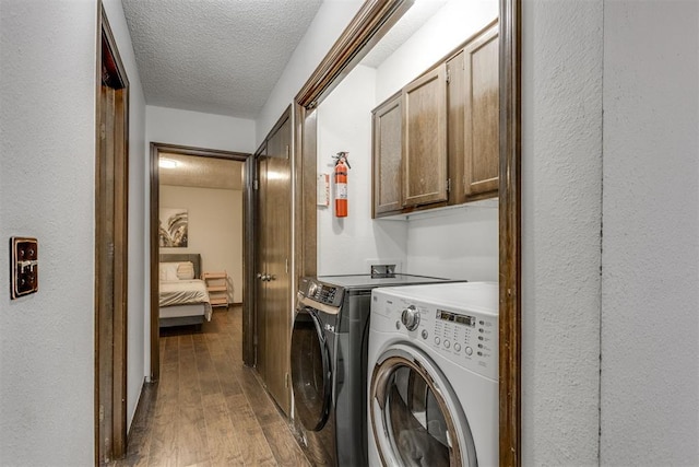 washroom with a textured ceiling, wood finished floors, washing machine and dryer, and cabinet space