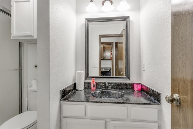 bathroom with toilet, a textured wall, and vanity