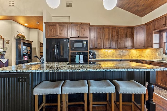 kitchen with visible vents, black appliances, a breakfast bar, and vaulted ceiling