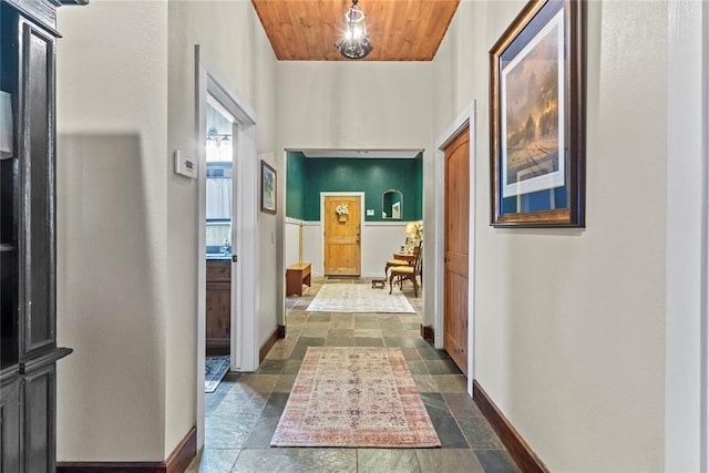 corridor featuring stone tile floors, wood ceiling, and baseboards