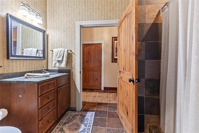 bathroom with wallpapered walls, stone tile floors, vanity, and a tile shower