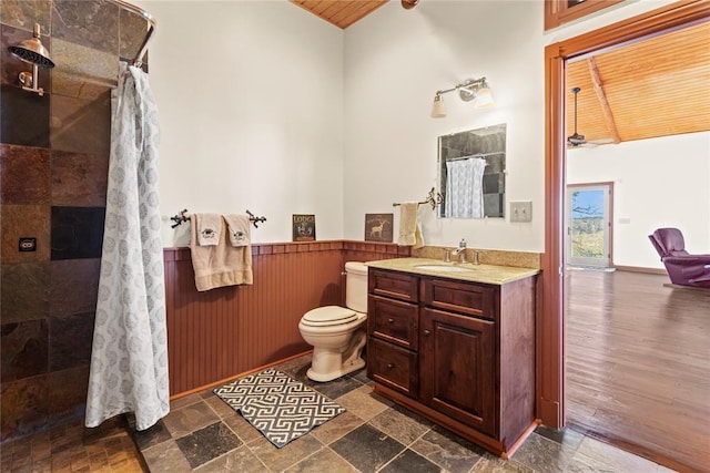 full bath featuring tiled shower, toilet, stone tile floors, and wainscoting