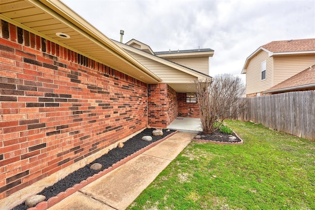 doorway to property with brick siding, a lawn, and fence