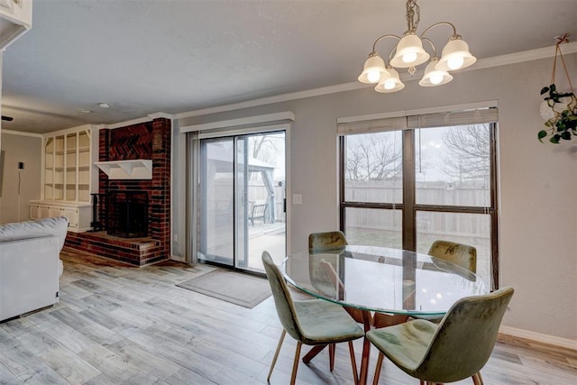 dining area with baseboards, a fireplace, ornamental molding, a notable chandelier, and light wood-type flooring