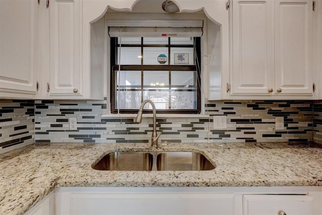 kitchen with white cabinets, light stone countertops, backsplash, and a sink