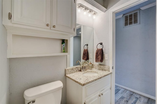 bathroom featuring visible vents, toilet, wood finished floors, baseboards, and vanity