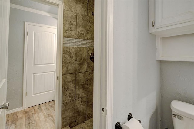 bathroom featuring toilet, wood finished floors, a textured wall, and tiled shower