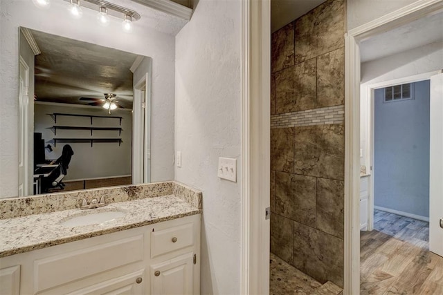 full bathroom with visible vents, wood finished floors, tiled shower, ceiling fan, and vanity