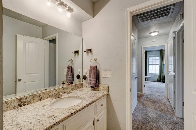 bathroom featuring visible vents, vanity, and a textured wall