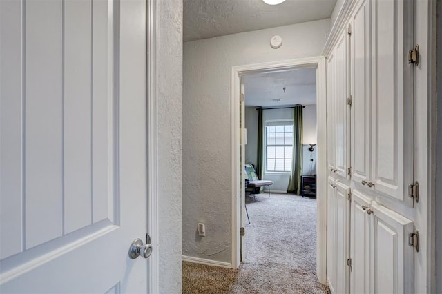 corridor with a textured wall, carpet floors, and a textured ceiling