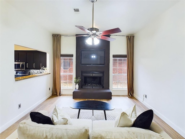 living area featuring a ceiling fan, light wood-type flooring, a large fireplace, and visible vents