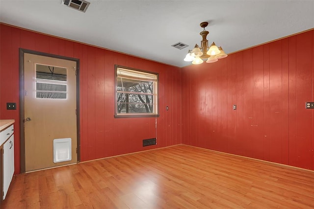 unfurnished dining area with light wood-type flooring, visible vents, and a notable chandelier