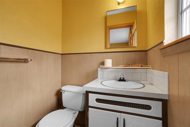 half bath with a wainscoted wall, vanity, and toilet