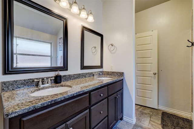 full bathroom featuring double vanity, stone finish floor, baseboards, and a sink