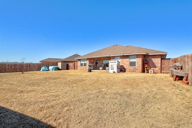 rear view of house with brick siding, a fenced backyard, and a lawn