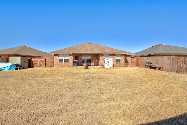 back of house featuring a gate, fence, brick siding, and a yard