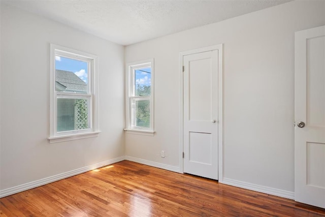 empty room with a textured ceiling, light wood-type flooring, and baseboards