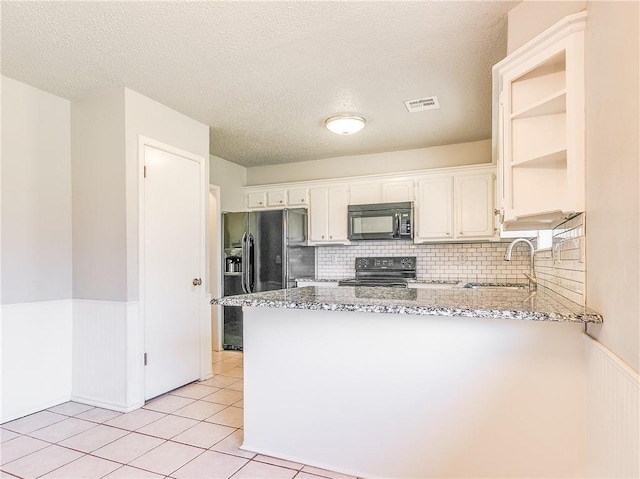 kitchen with a wainscoted wall, black appliances, a peninsula, and a sink