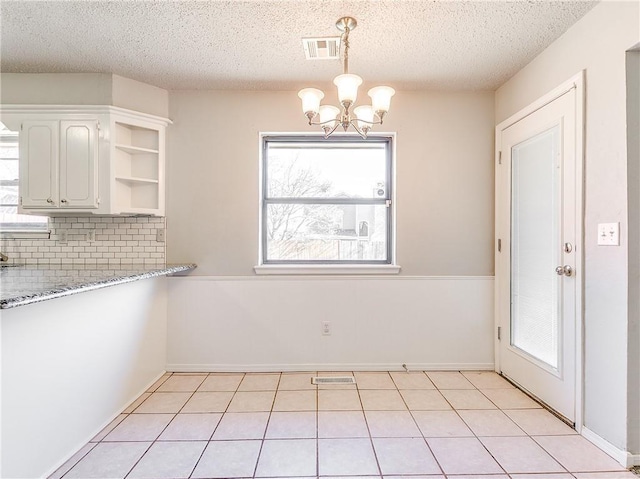 unfurnished dining area with a textured ceiling, visible vents, a notable chandelier, and light tile patterned flooring