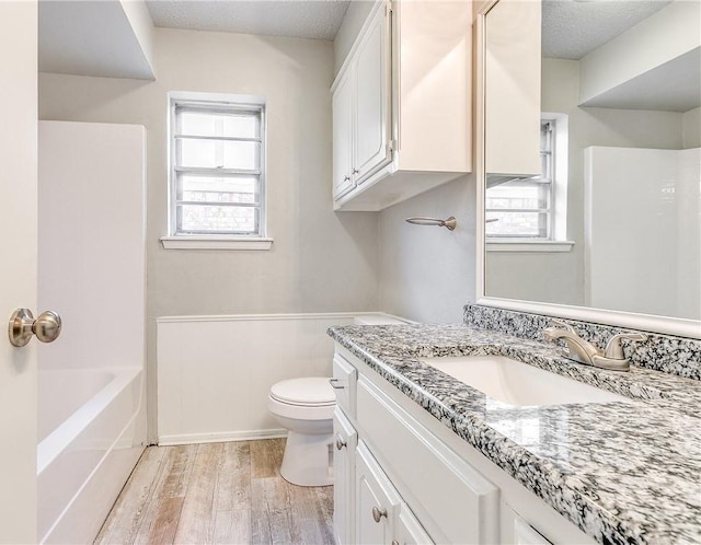 full bath featuring toilet, a textured ceiling, wood finished floors, and vanity