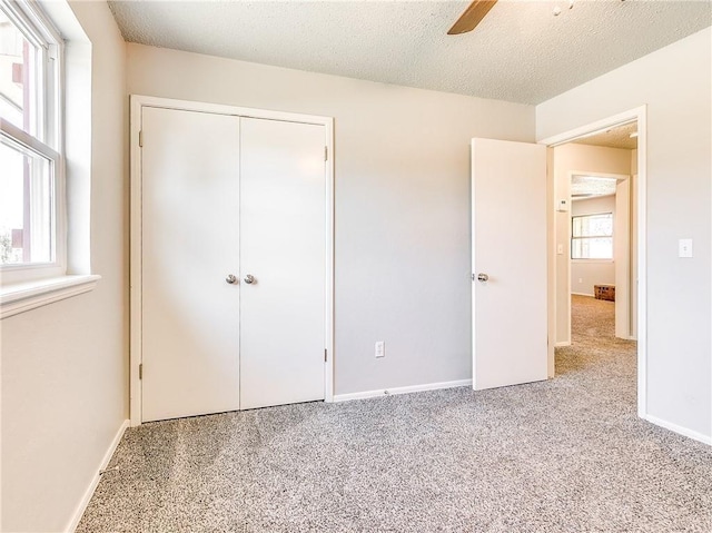 unfurnished bedroom featuring a closet, a textured ceiling, baseboards, and carpet flooring