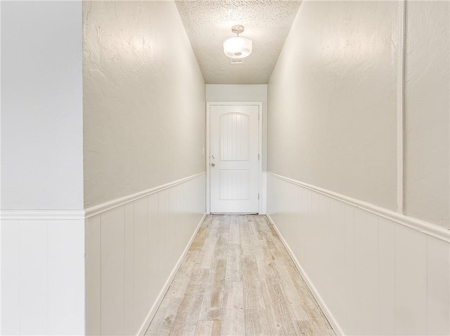 hall featuring wainscoting, a textured ceiling, and wood finished floors