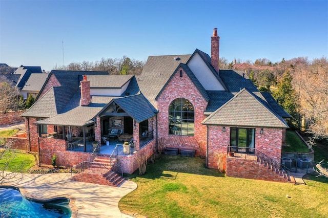 tudor house with brick siding, a front yard, a chimney, and a patio area