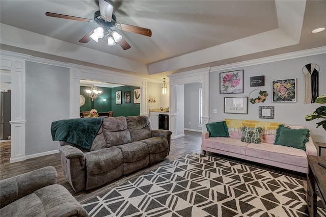 living area featuring ceiling fan with notable chandelier, baseboards, a tray ceiling, and ornamental molding