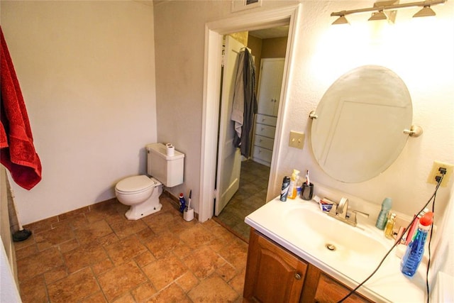 bathroom featuring vanity, stone finish floor, toilet, and baseboards