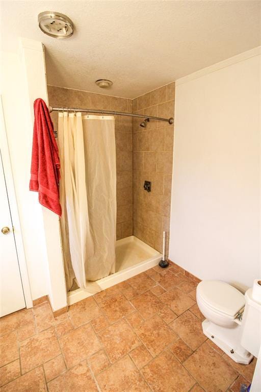 bathroom featuring toilet, a stall shower, stone finish flooring, a textured ceiling, and baseboards