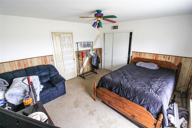 carpeted bedroom featuring a ceiling fan, visible vents, a wainscoted wall, and wood walls