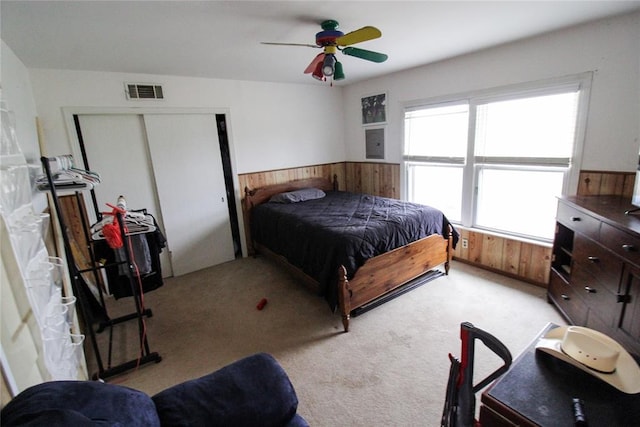 bedroom featuring visible vents, a wainscoted wall, wood walls, light colored carpet, and a closet