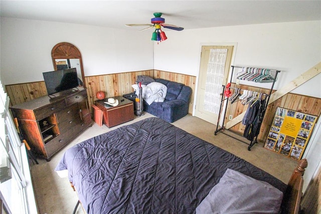 bedroom with a wainscoted wall, wood walls, carpet flooring, and a ceiling fan