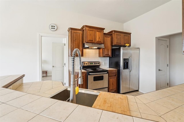 kitchen with under cabinet range hood, decorative backsplash, tile countertops, and appliances with stainless steel finishes