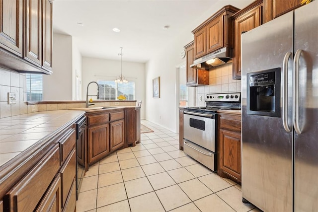 kitchen featuring tile counters, under cabinet range hood, light tile patterned flooring, stainless steel appliances, and a sink