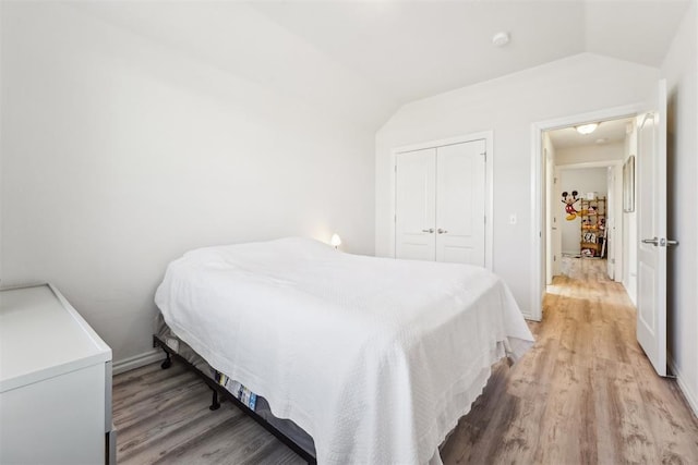 bedroom featuring a closet, light wood-style flooring, baseboards, and lofted ceiling