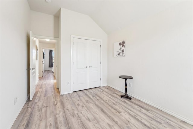 unfurnished bedroom with a closet, baseboards, light wood-style floors, and vaulted ceiling